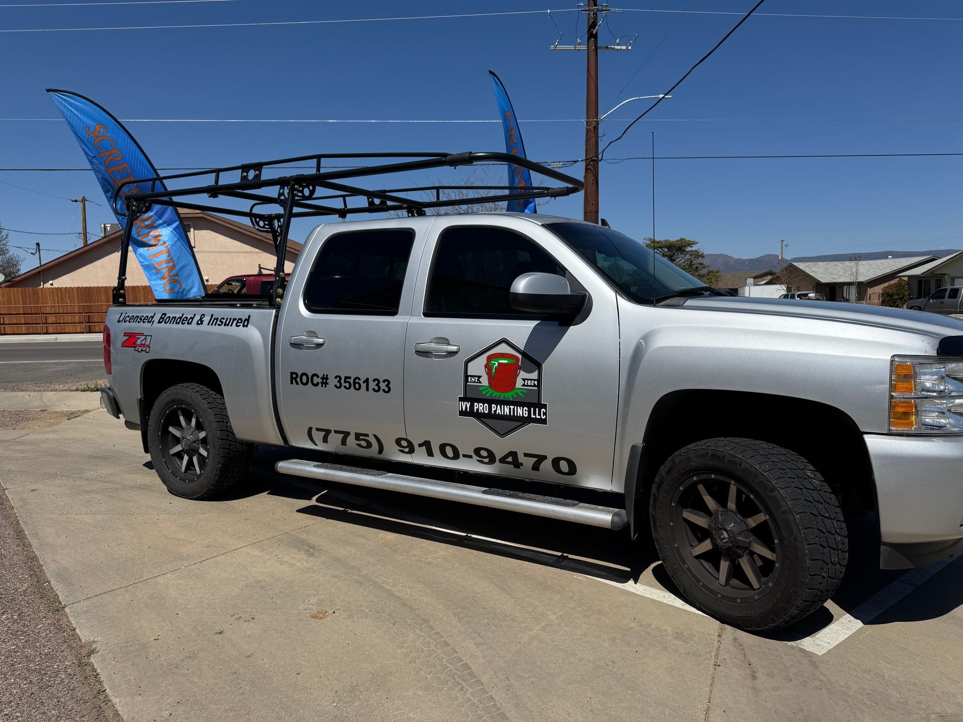 Silver pickup truck with roof rack and company logo, parked on a sunny day.