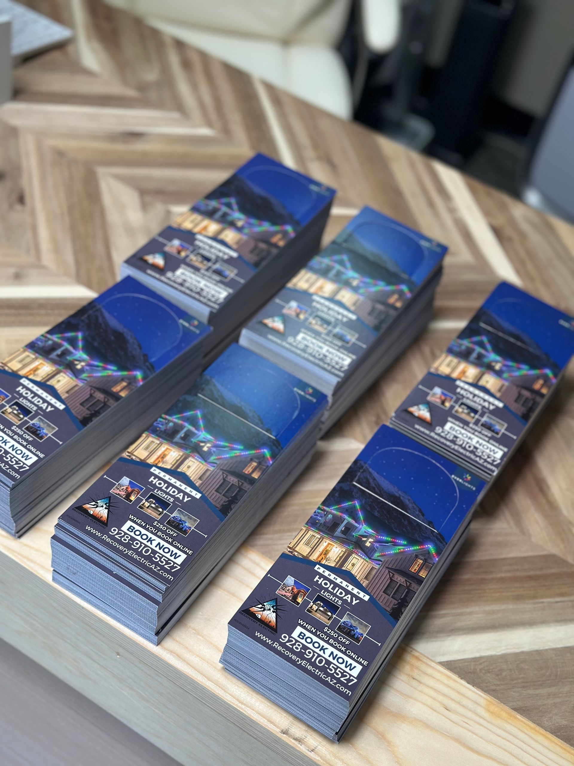 Four stacks of printed promotional materials on a wooden table. Each piece has a blue and black image.