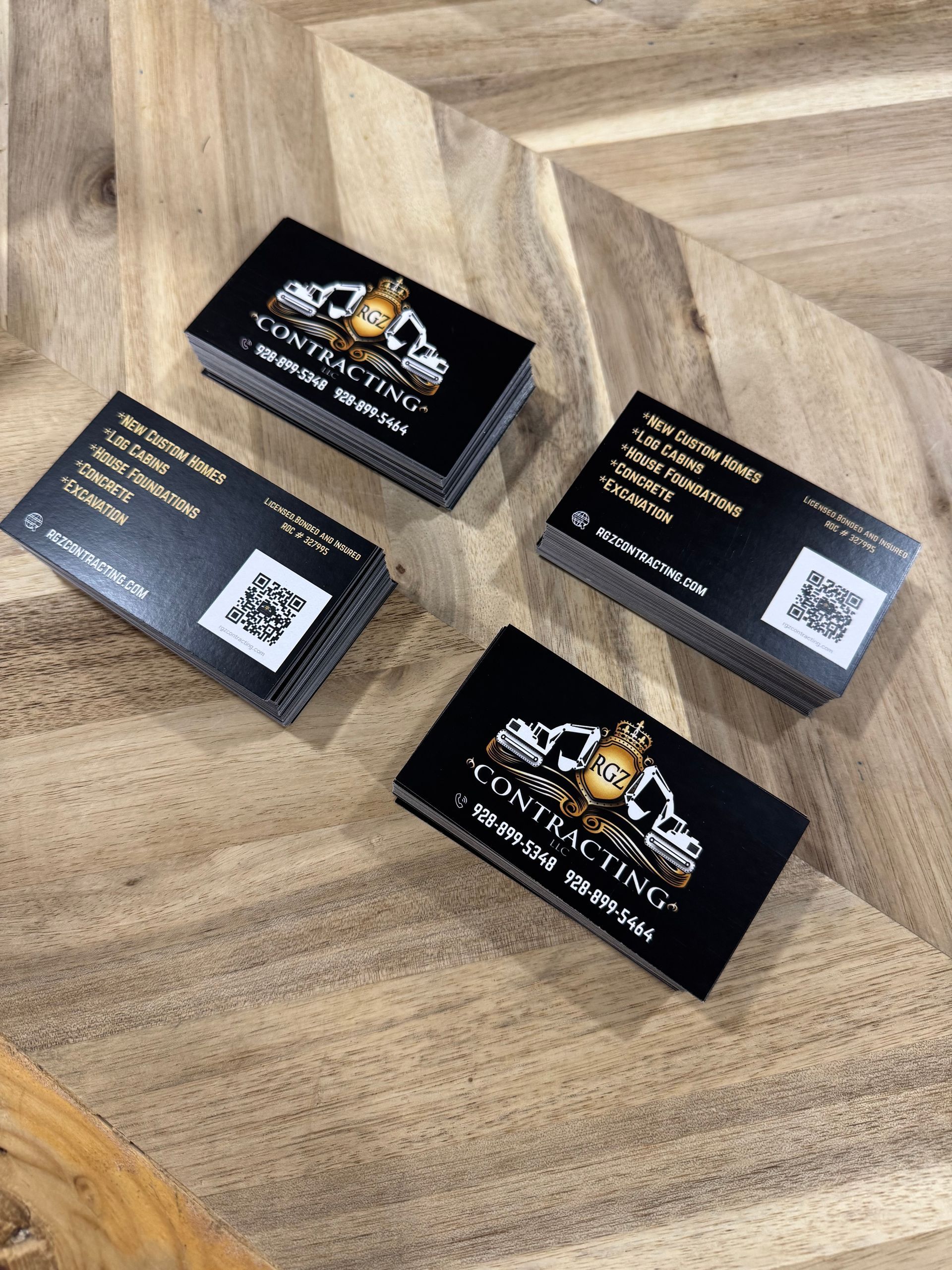 Four black business cards with gold lettering on a wooden surface.