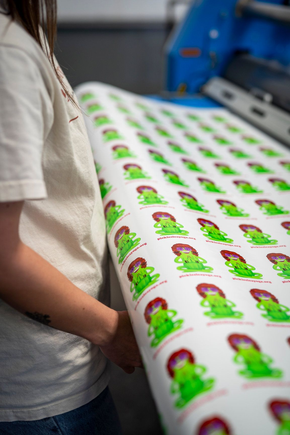 Person rolls a sheet of stickers with a green cartoon character on a printing machine.