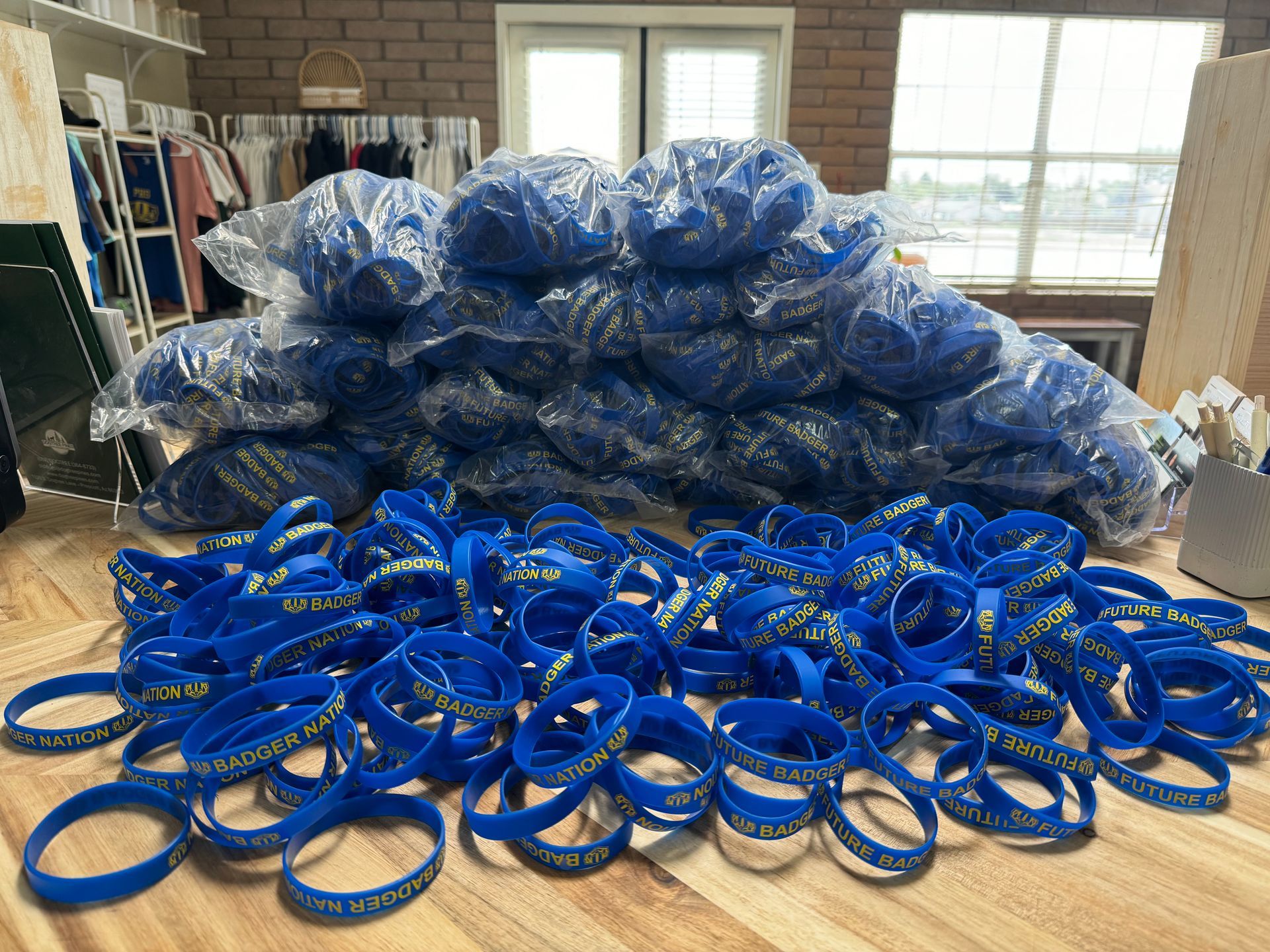 Blue wristbands with gold text, piled and in clear plastic, inside a room.
