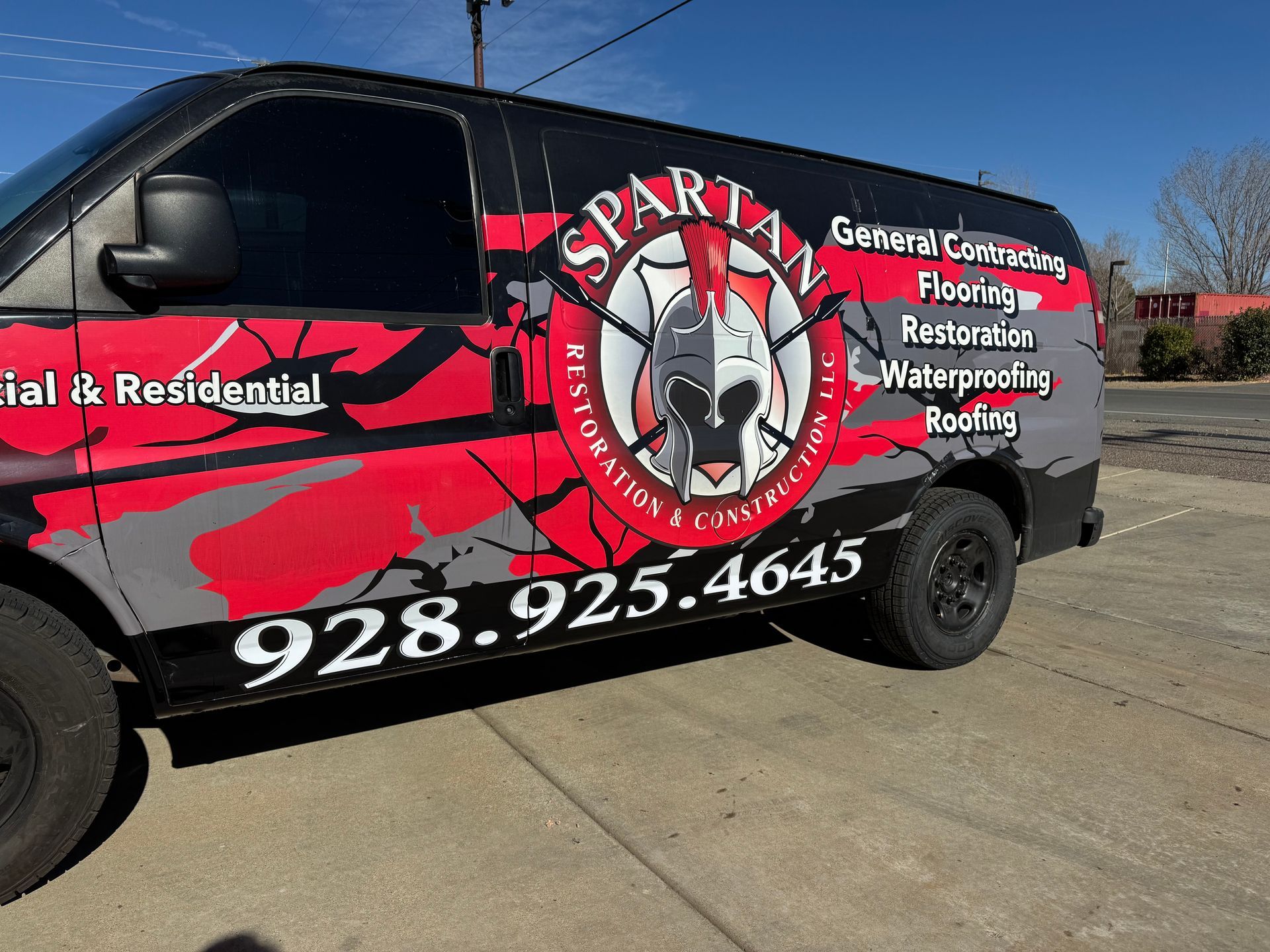 Spartan Restoration van with logo and phone number, parked outdoors. Black, red, and gray colors.