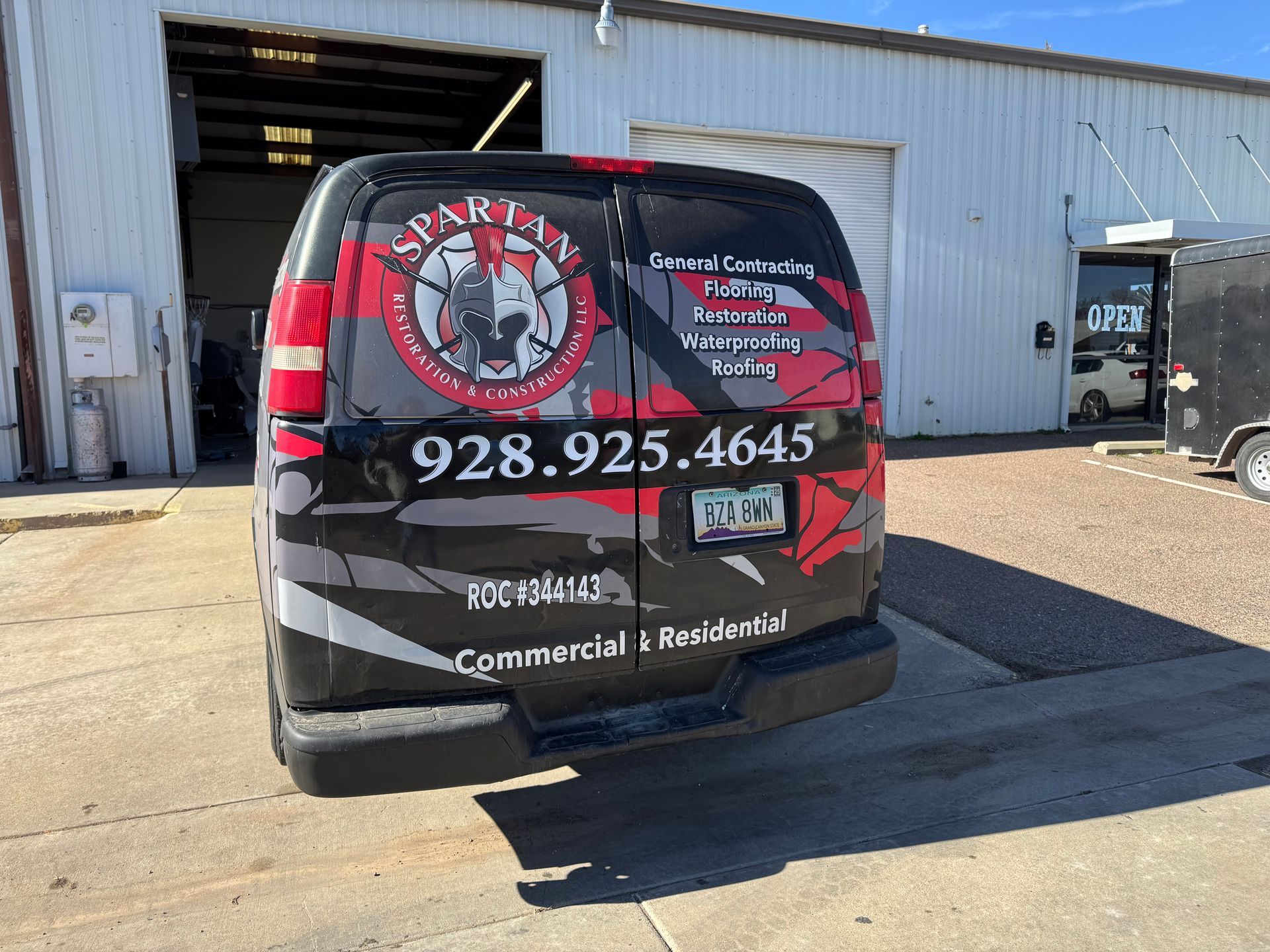 Black van with Spartan logo, phone number, and business services advertised. Parked outside a building.