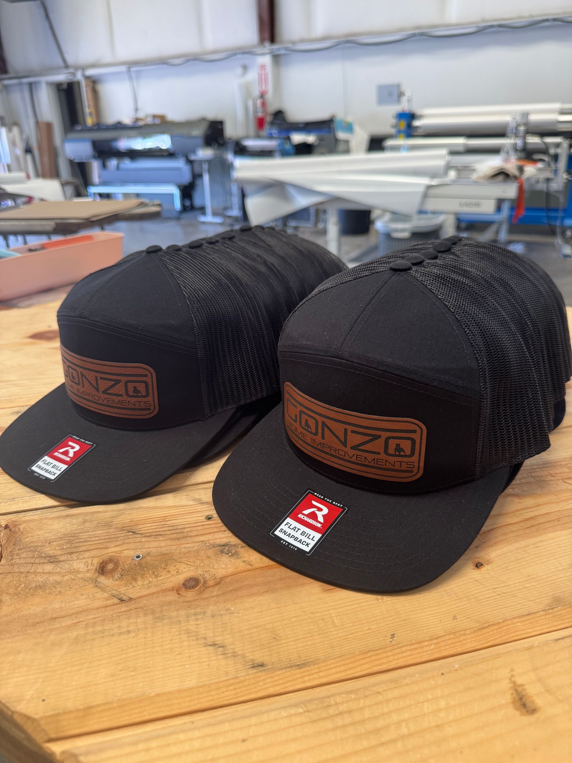 Two black trucker hats with brown leather patches on a wood surface, indoors.