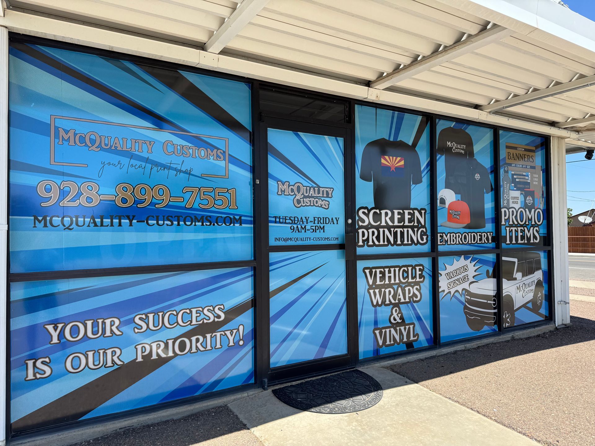 A storefront with blue and white graphics advertising screen printing, vehicle wraps, and promotional items.