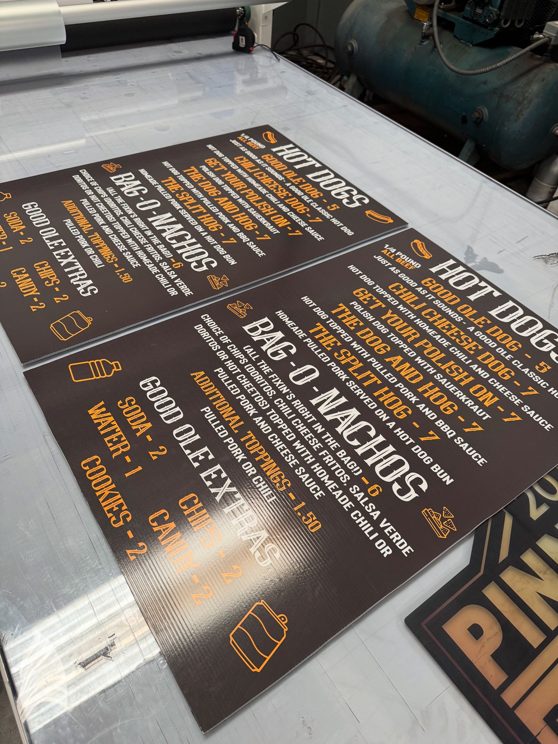 Printed food menus, brown with white and orange text, sit on a large printing machine.