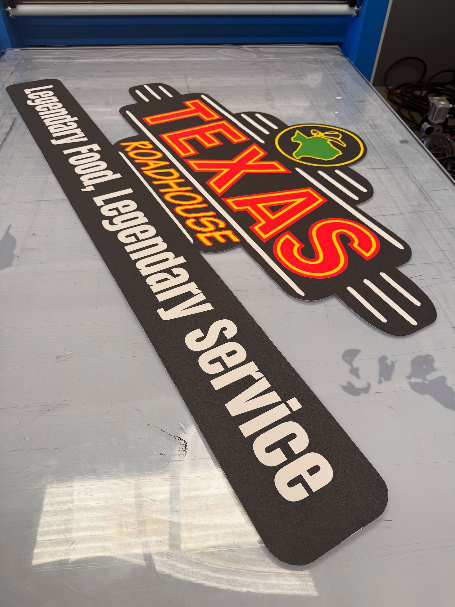 Texas Roadhouse logo and tagline mats on a metal surface. Black and white text, red and yellow logo.