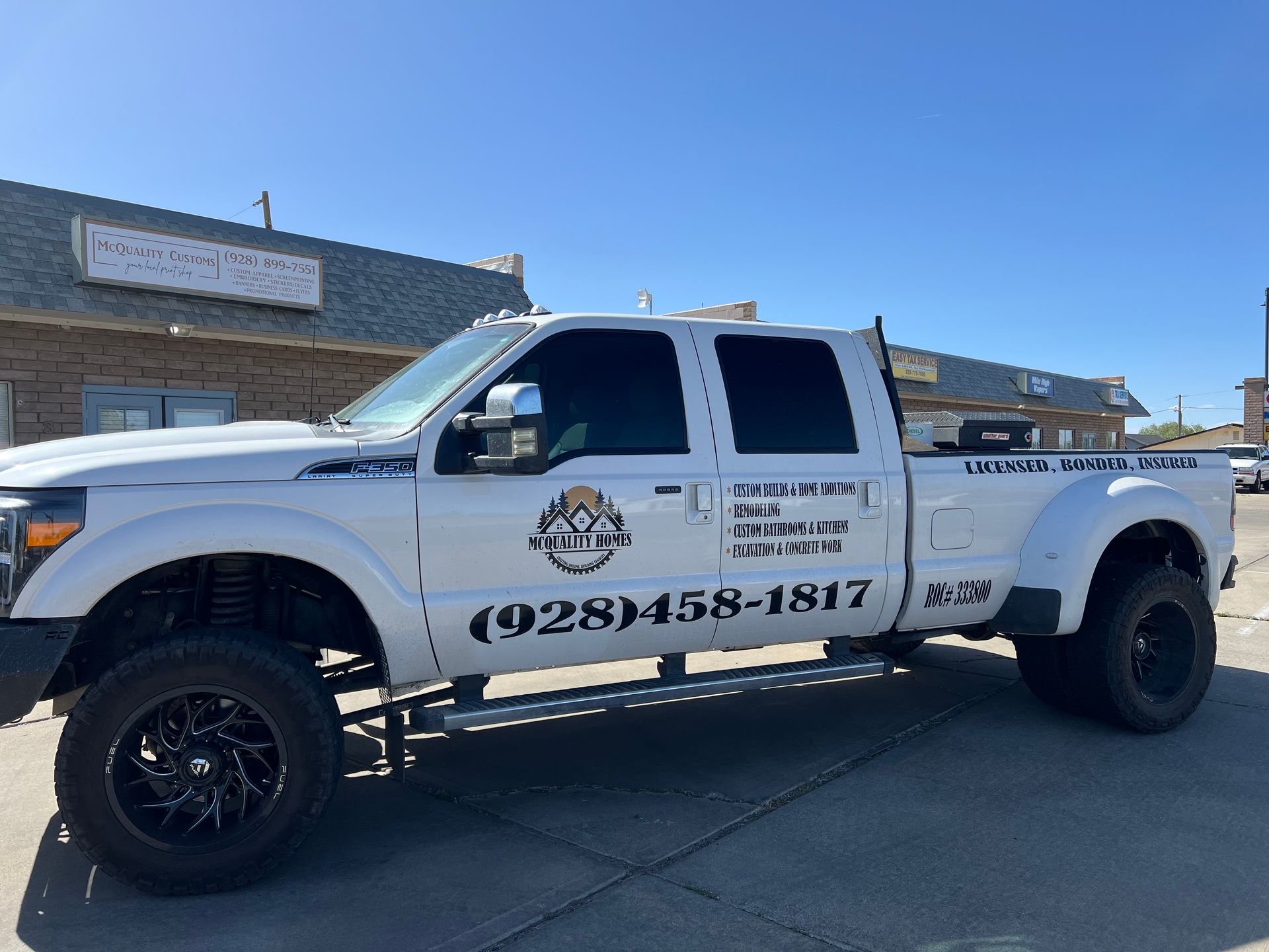 White pickup truck with company logo and phone number parked in front of a building.