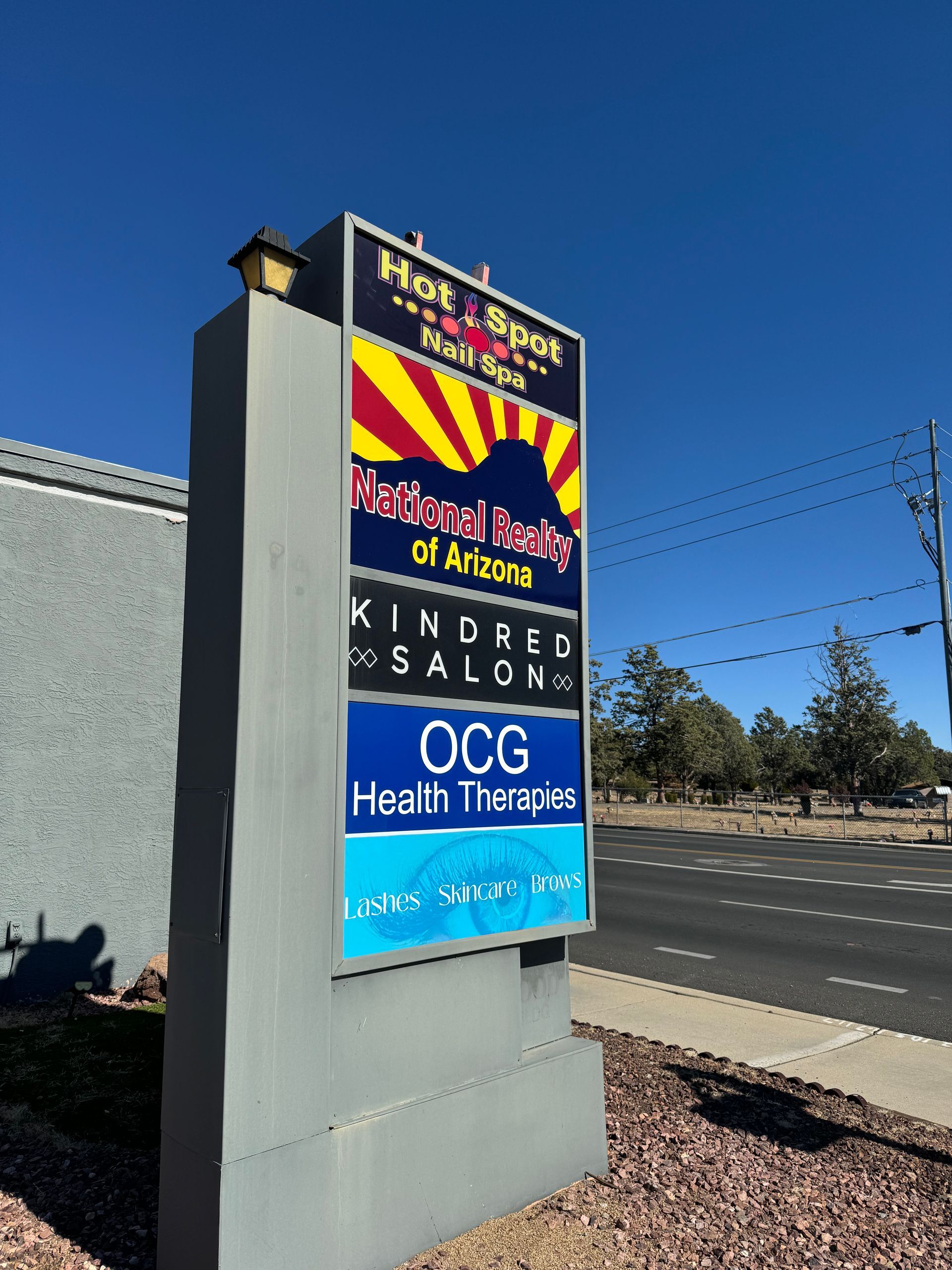 Sign with business names: Hot Spot Tanning, High Desert Realty, Kindred Salon, OCG Health Therapies. Arizona sky.