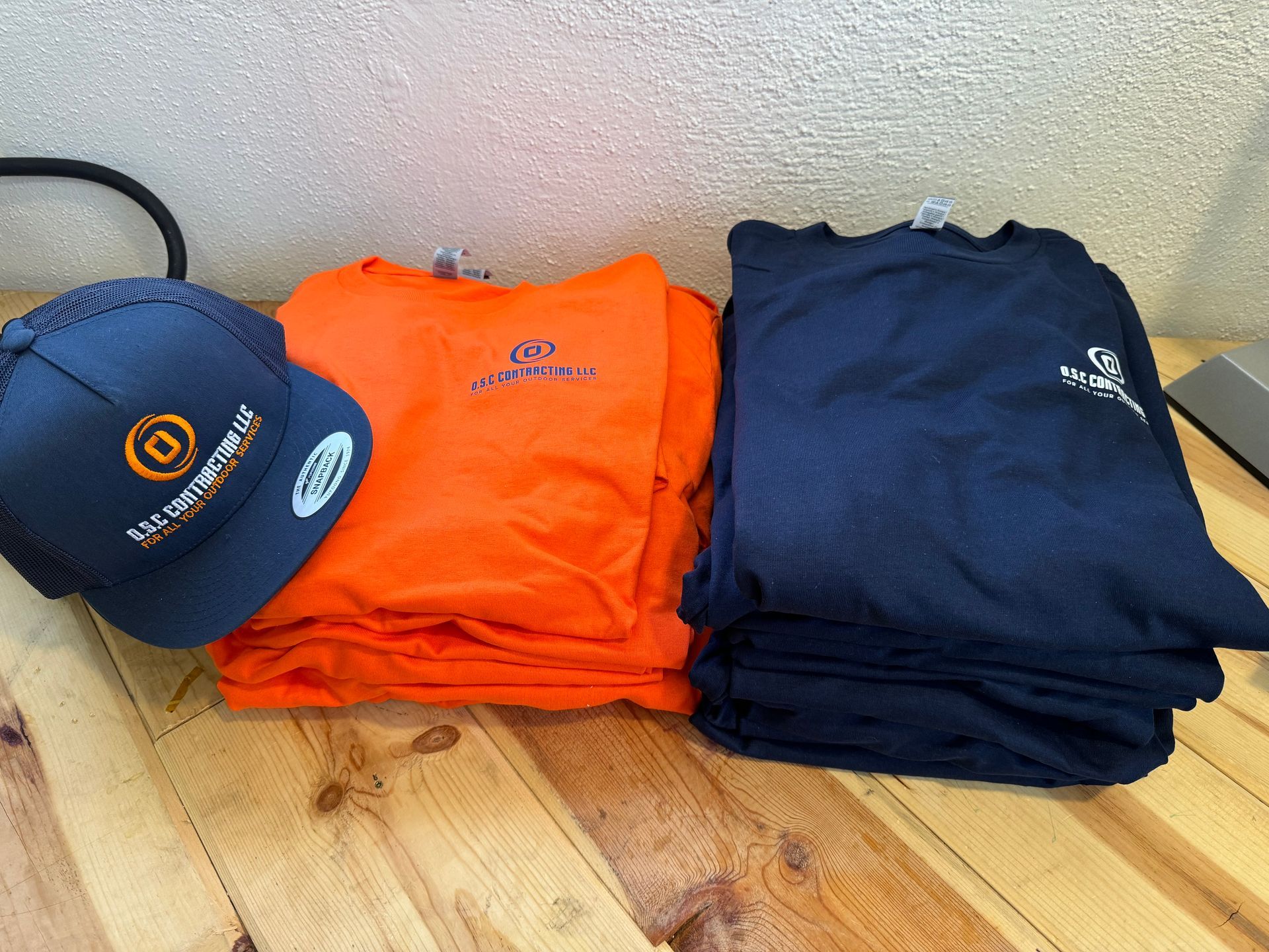 A hat, orange and navy shirts with a logo stacked on a wooden surface.