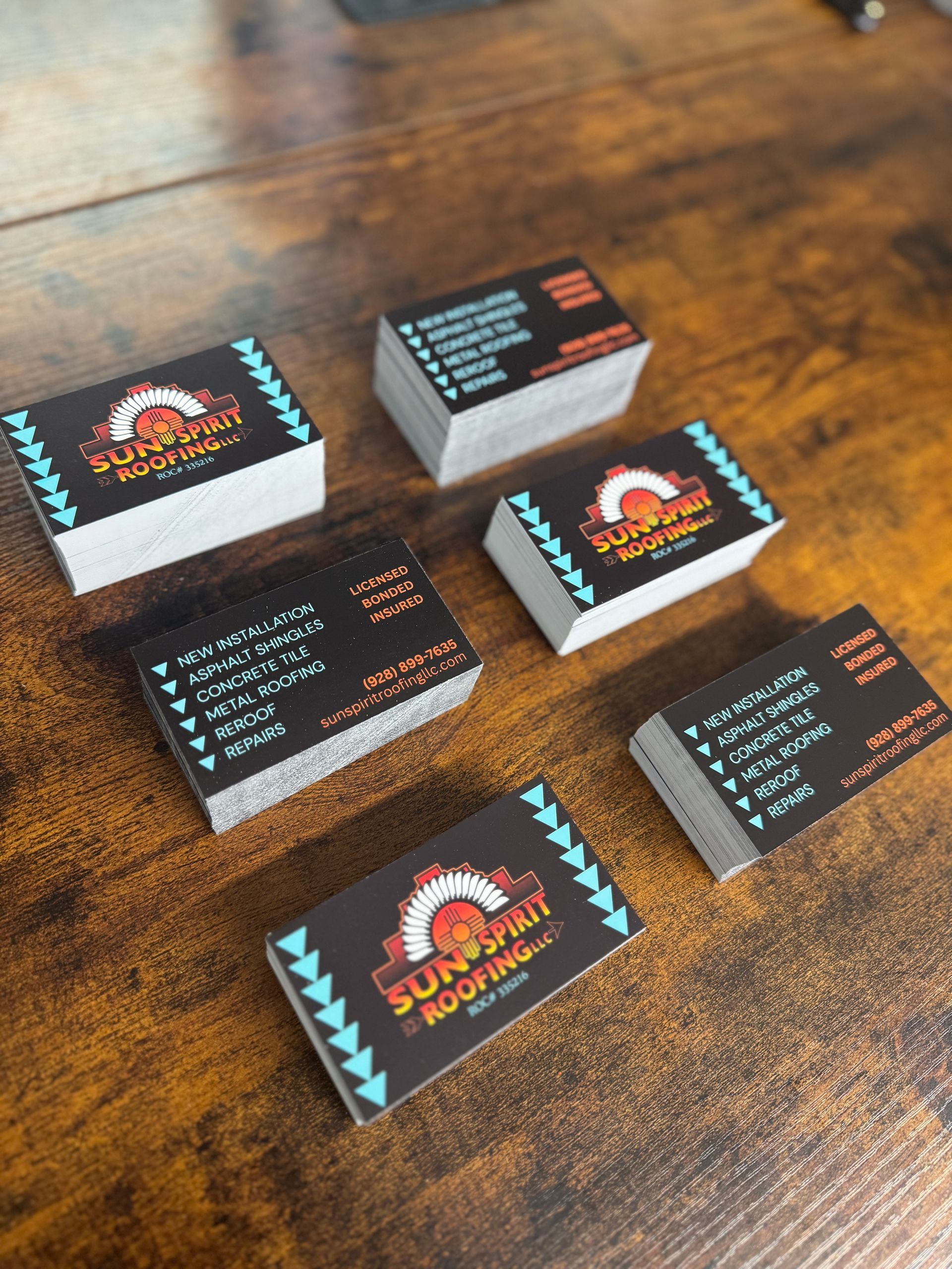 Stacks of business cards on a brown wooden surface. They have a black background with orange and teal details.