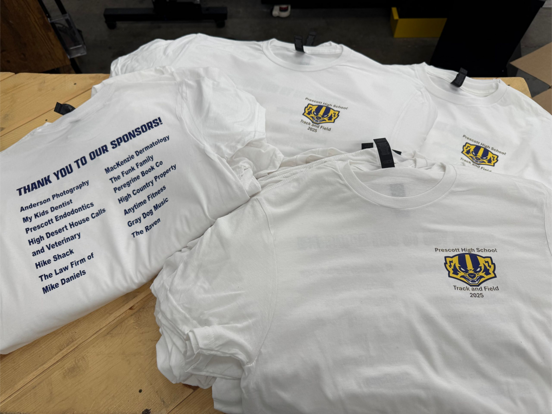 White t-shirts with sponsor names and logo stacked on a table.