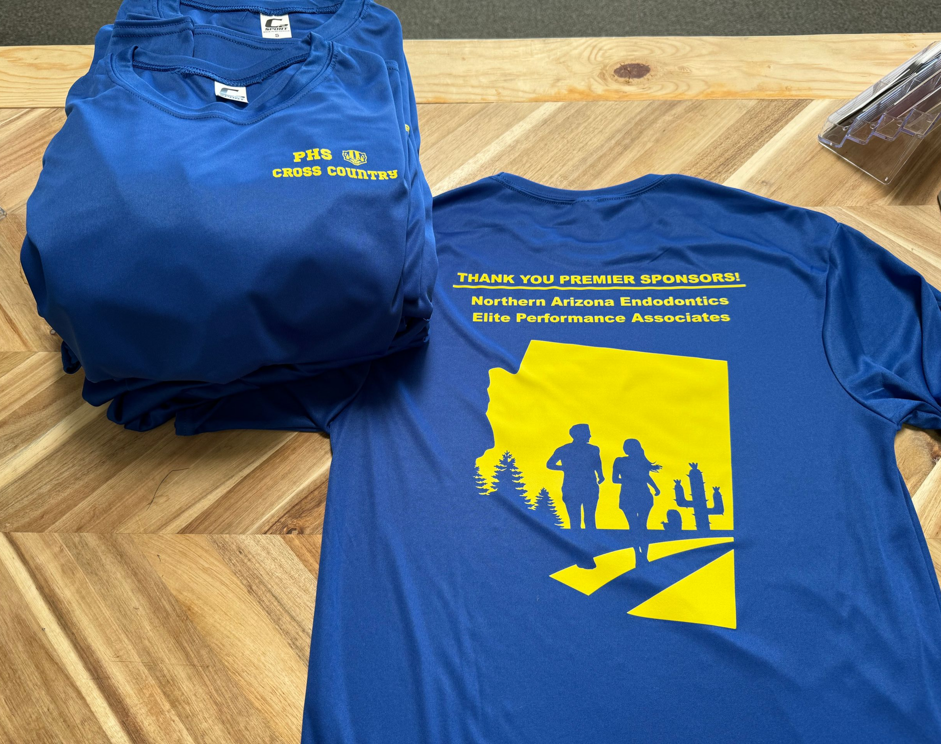 Blue t-shirts stacked, one showing back with Arizona graphic, thanking sponsors.