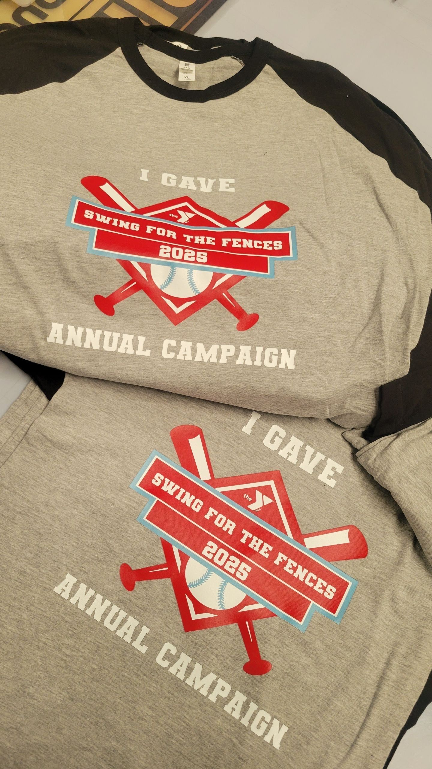 Two gray baseball shirts with red and white text, featuring the slogan
