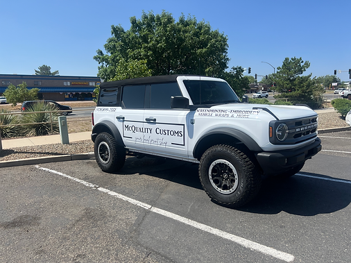 White Ford Bronco with black accents parked in a parking space in front of a building, under a sunny sky.