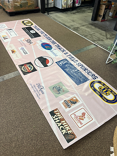 Pink banner listing track & field sponsors, with various logos, on a brown carpeted floor.