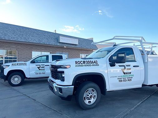 Two white work trucks parked in front of a building. One has a ladder rack. Both have company logos and text.