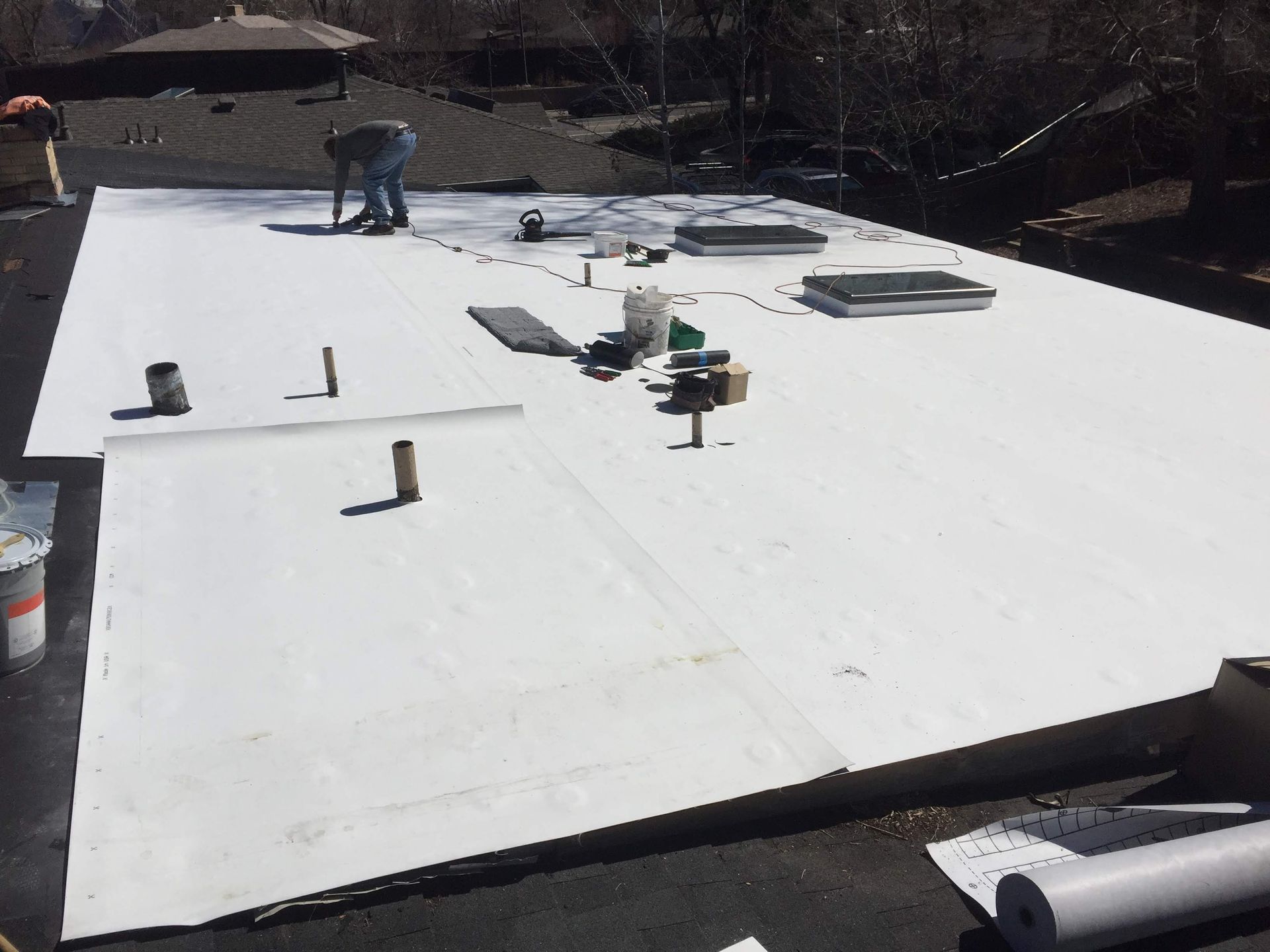 Man working on a white flat roof, surrounded by tools and materials.