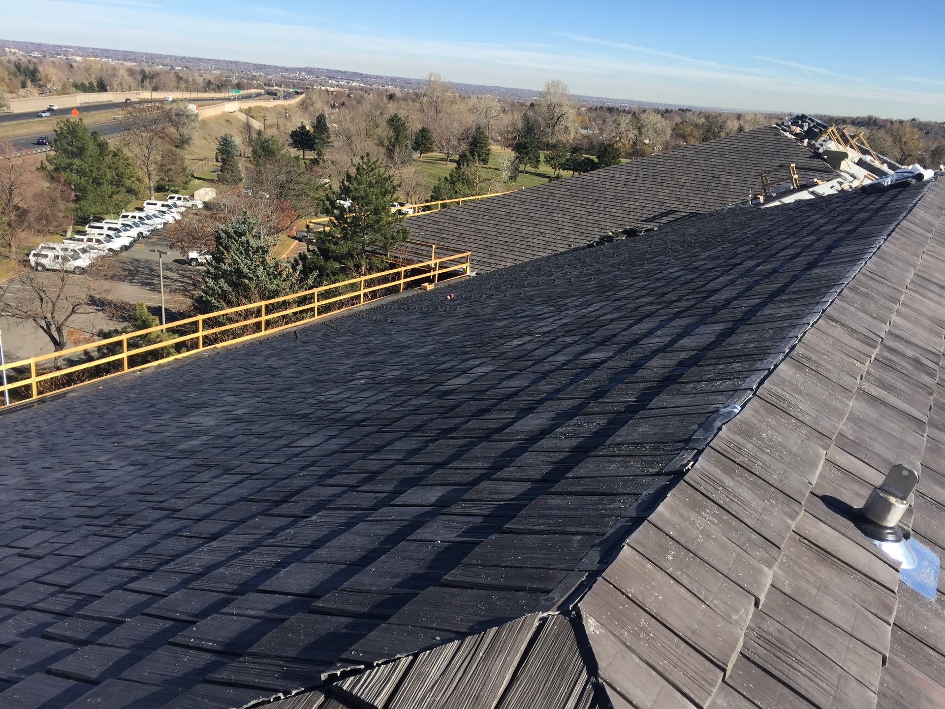 A roof with shingles and a black strip in the center, overlooking a landscape with a fence.