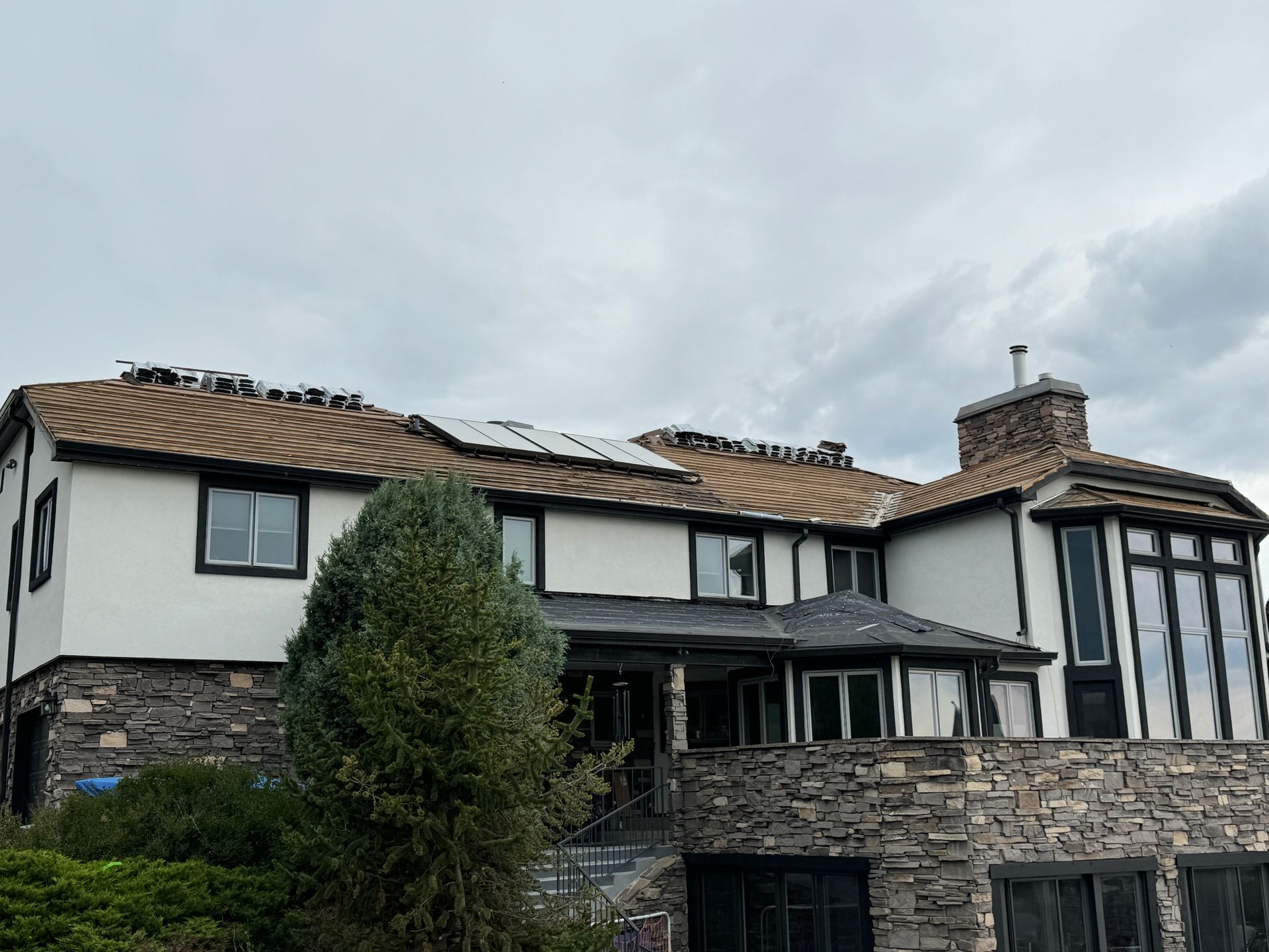 House with roof partially under construction, cloudy sky. White exterior with stone and dark trim.