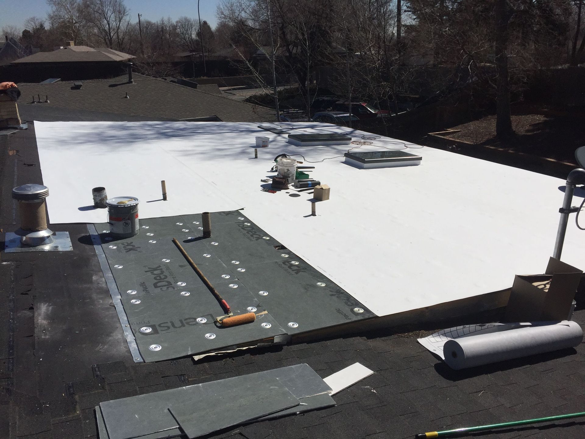 Flat roof being repaired with white membrane. Tools and materials are scattered on the roof.
