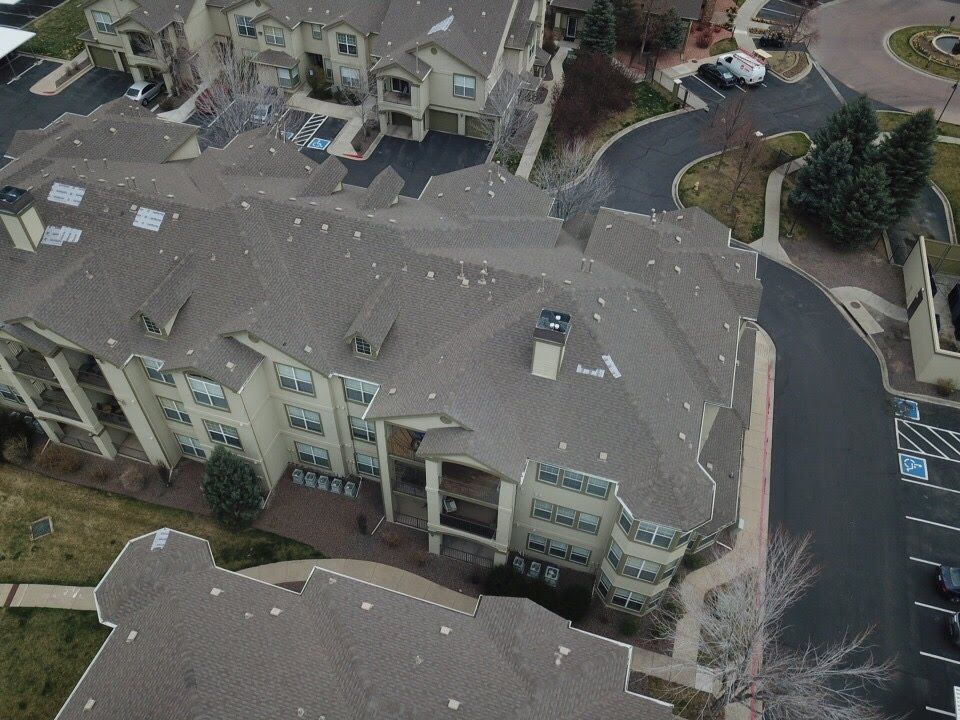 Aerial view of a large, beige apartment complex with brown rooftops, surrounded by roads and trees.