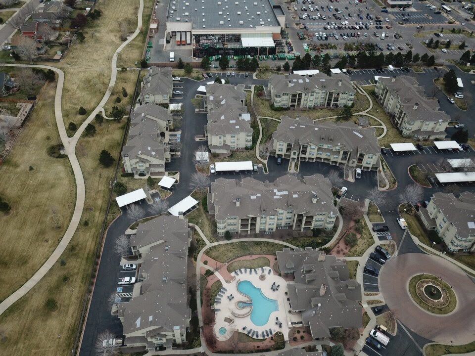 Aerial view of an apartment complex with a pool, parking lots, and a large retail store in the background.