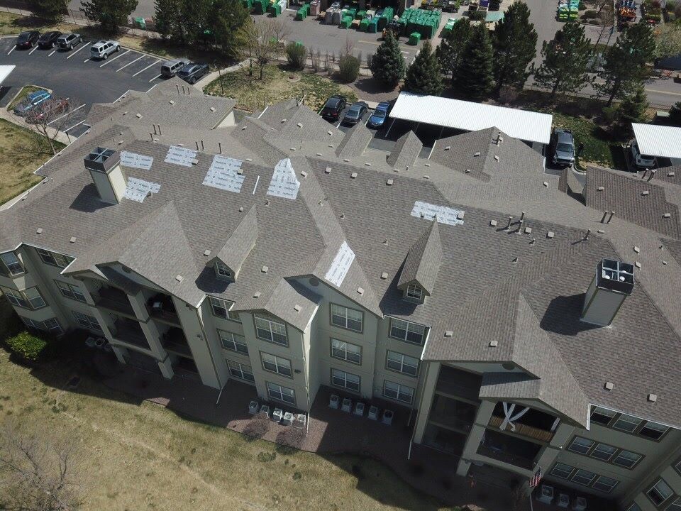 Aerial view of a multi-story apartment building with a brown roof and multiple vent stacks.