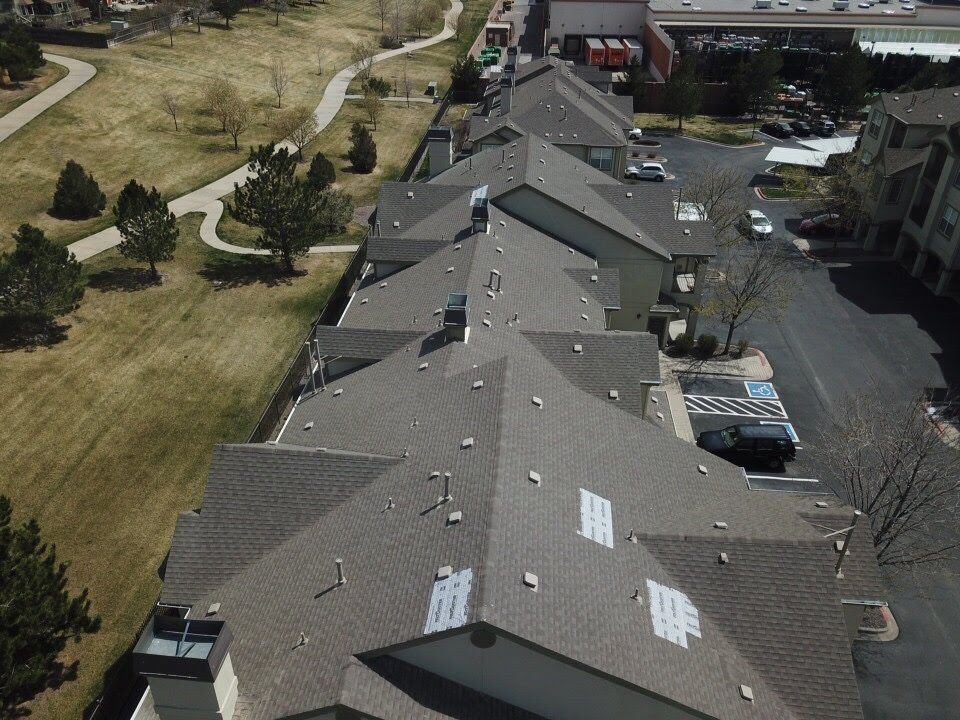 Overhead view of townhouses with dark gray roofs, next to a park with a walking path and trees.