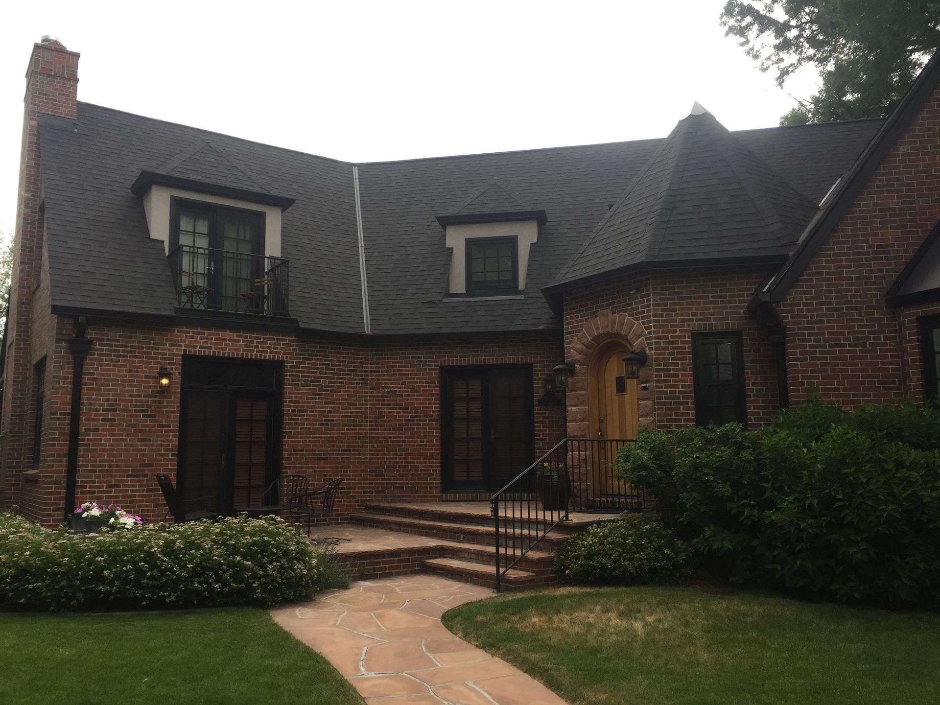 Brick house with dark roof, black trim, arched doorway, and stone path leading to the front.