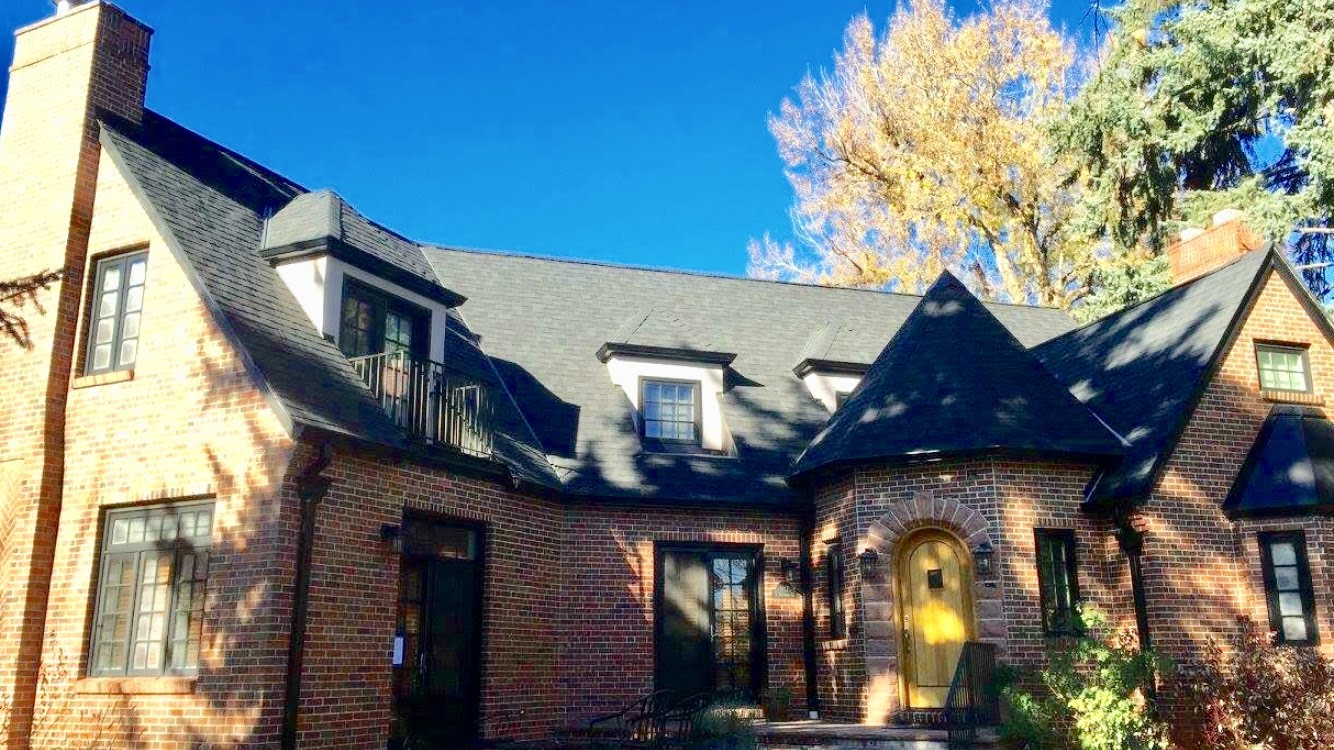 Brick house with black roof and windows under a clear blue sky.