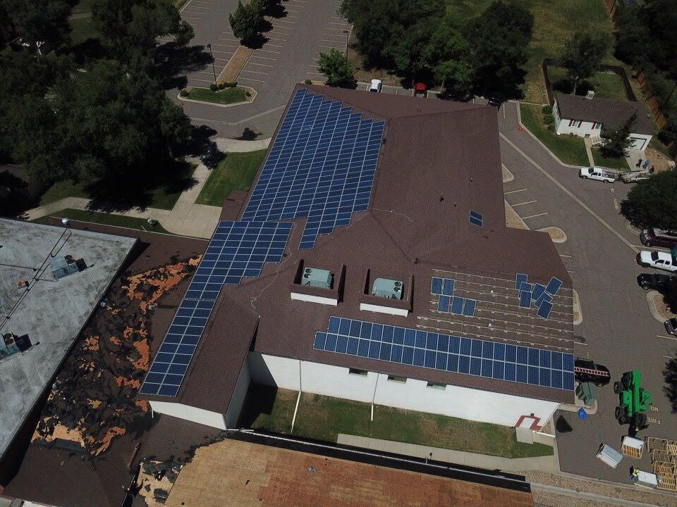 Solar panels on a brown roof, building with white walls, green lawn, cars parked nearby.