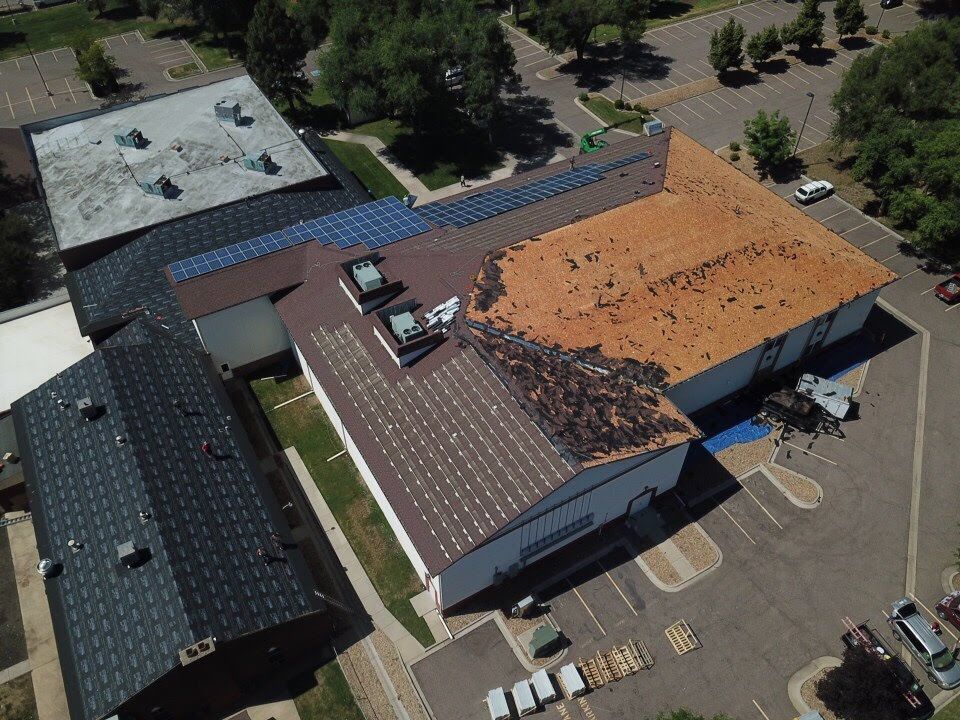 Aerial view of a building with multiple roof sections, some with solar panels, and a damaged brown roof.