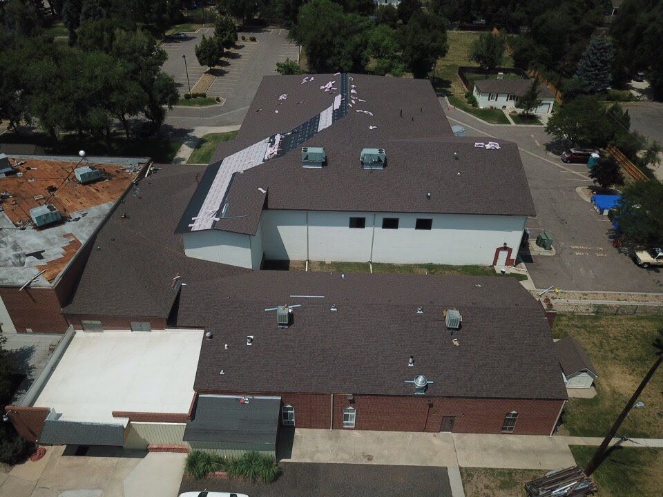 An aerial view of a brown-roofed building complex with parking and surrounding trees.