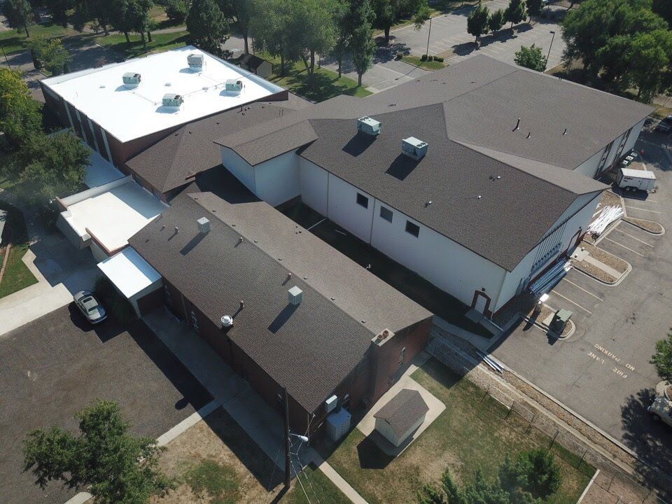 Aerial view of a white building with brown roofs and paved parking. Sunny, outdoor setting.
