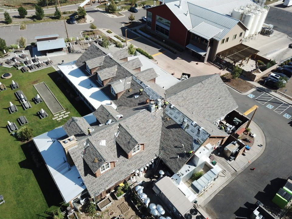 Aerial view of a brewery with outdoor seating, featuring a brown shingled roof and green lawn.