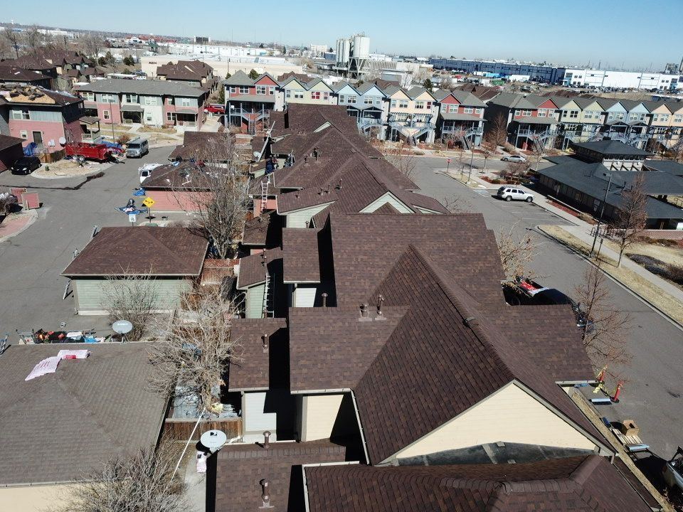 Brown-roofed townhomes in a residential area on a sunny day, with a cityscape in the background.
