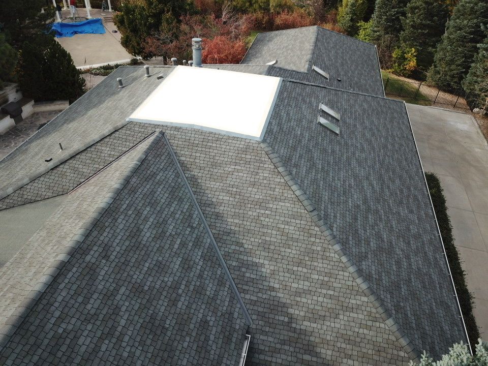 Overhead view of a house with asphalt shingle roof and a white flat roof section; a driveway.