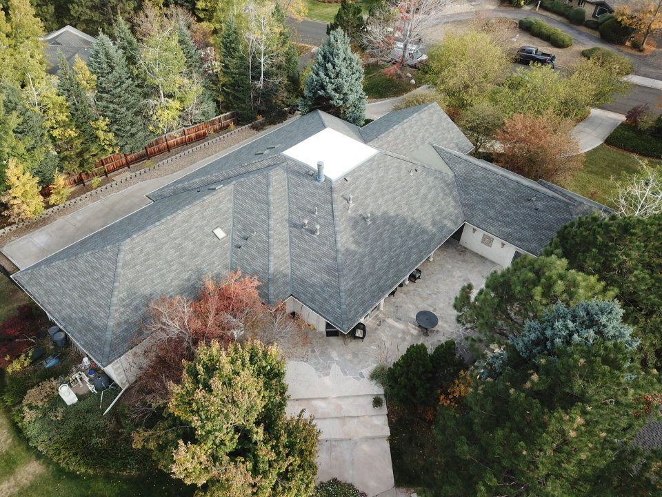 Aerial view of a house with a gray roof, surrounded by trees in fall colors; a patio is in front.