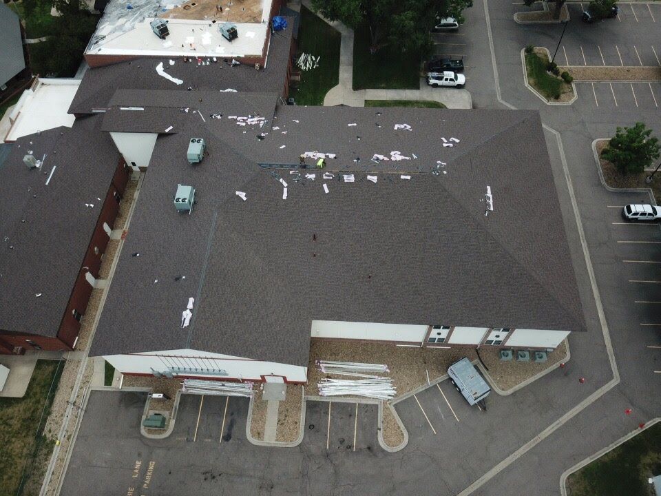 Aerial view of a building with dark brown roof, some shingles missing. White debris visible.
