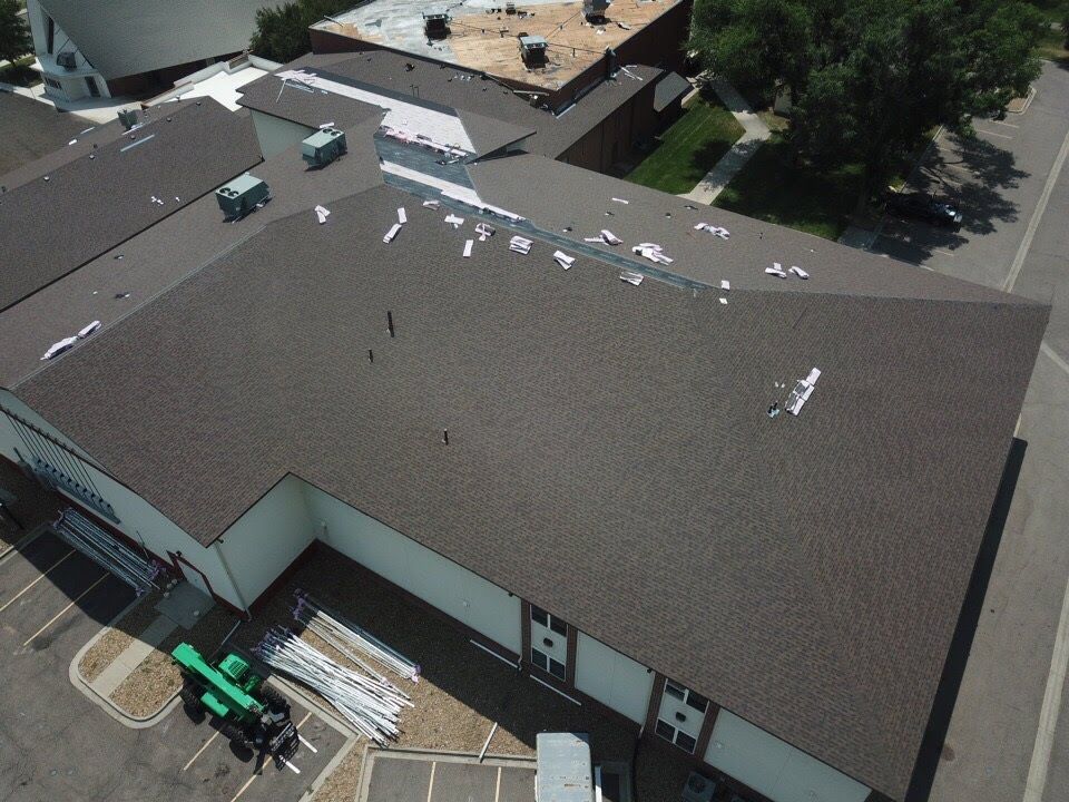 Aerial view of a building with a brown shingled roof and visible roofing work in progress.