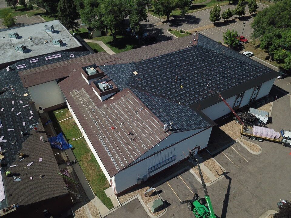 Aerial view of building roof repair: workers, equipment, brown and black roofing, blue tarp, sunny day.