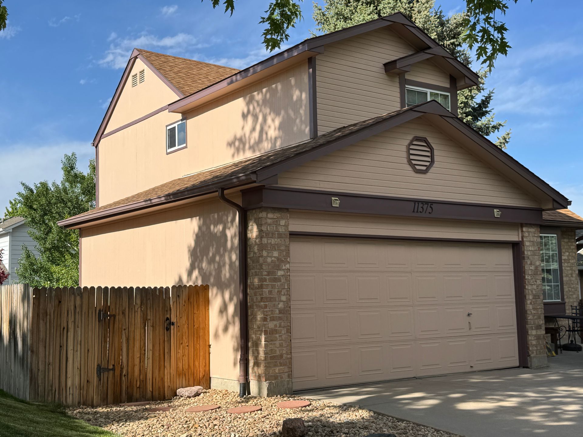 Tan two-story house with a garage, wooden fence, and blue sky.