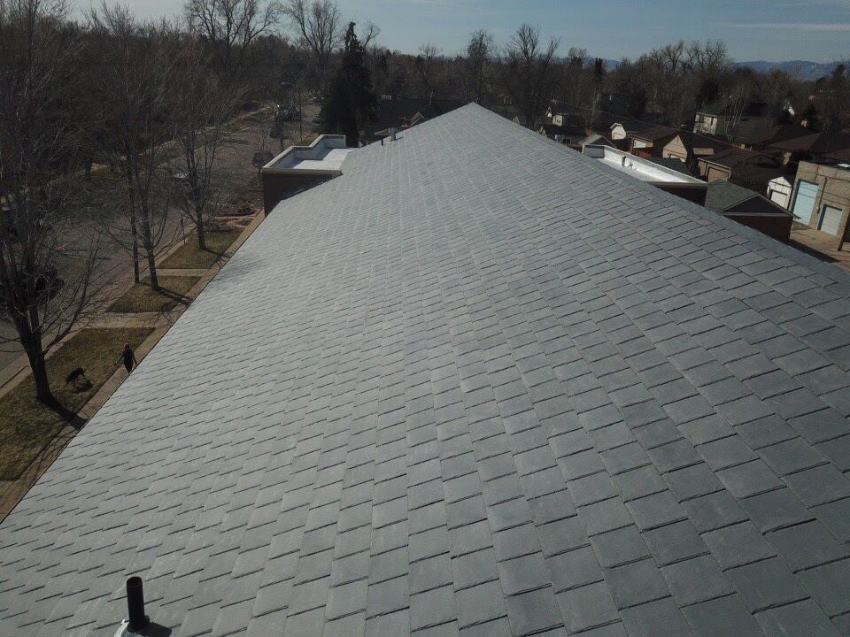 Gray asphalt shingle roof on a building, viewed from above. Trees and houses in the background.