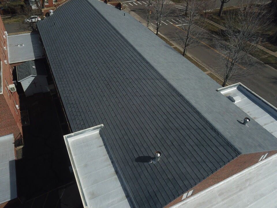 Aerial view of a long, dark gray shingle roof on a building with a white-trimmed roof.