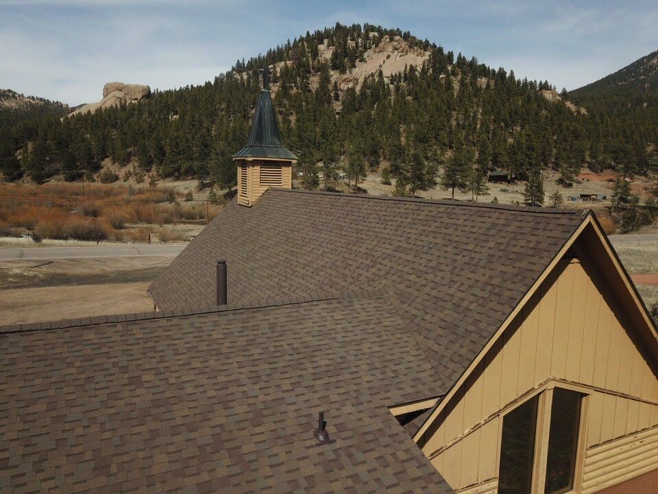 Brown shingled roof with steeple and mountains in the background.