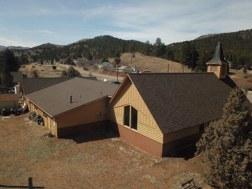 Church building with brown roof and steeple, mountains in background.