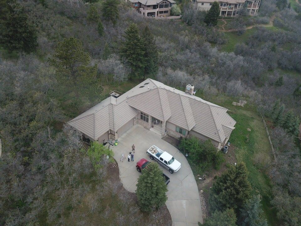 Overhead view of a house with a long driveway, a white truck parked near it, and trees in the background.
