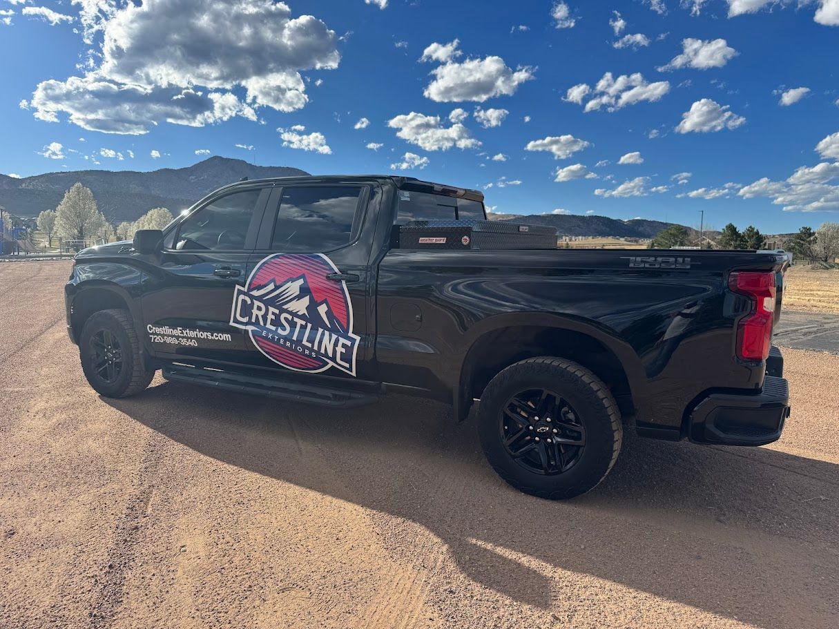 A black crew cab pickup truck with a Crestline logo on its side parked on a dirt road under a blue sky with clouds.