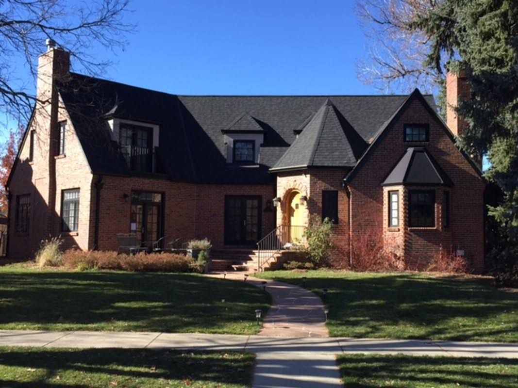 Brick house with black roof, turret, arched doorway, and front lawn under a blue sky.